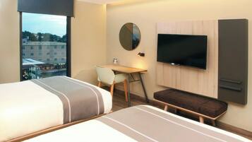 Habitación de hotel con cama, escritorio, silla, televisor y vista a la ciudad.