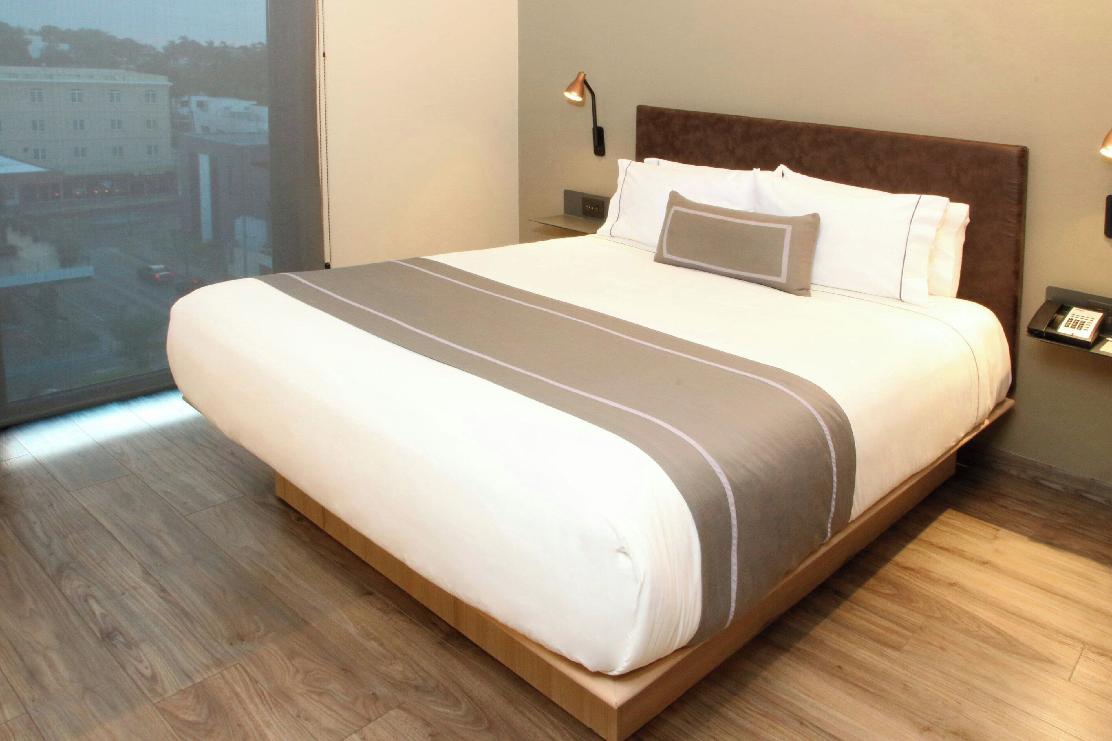 Ein modernes Hotelzimmer mit einem großen Bett, Blick auf die Stadt und Holzboden.