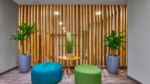 A modern interior with wooden slats, two potted plants, and two colorful seating areas. - City Express Plus by Marriott Tampico (Tampico)