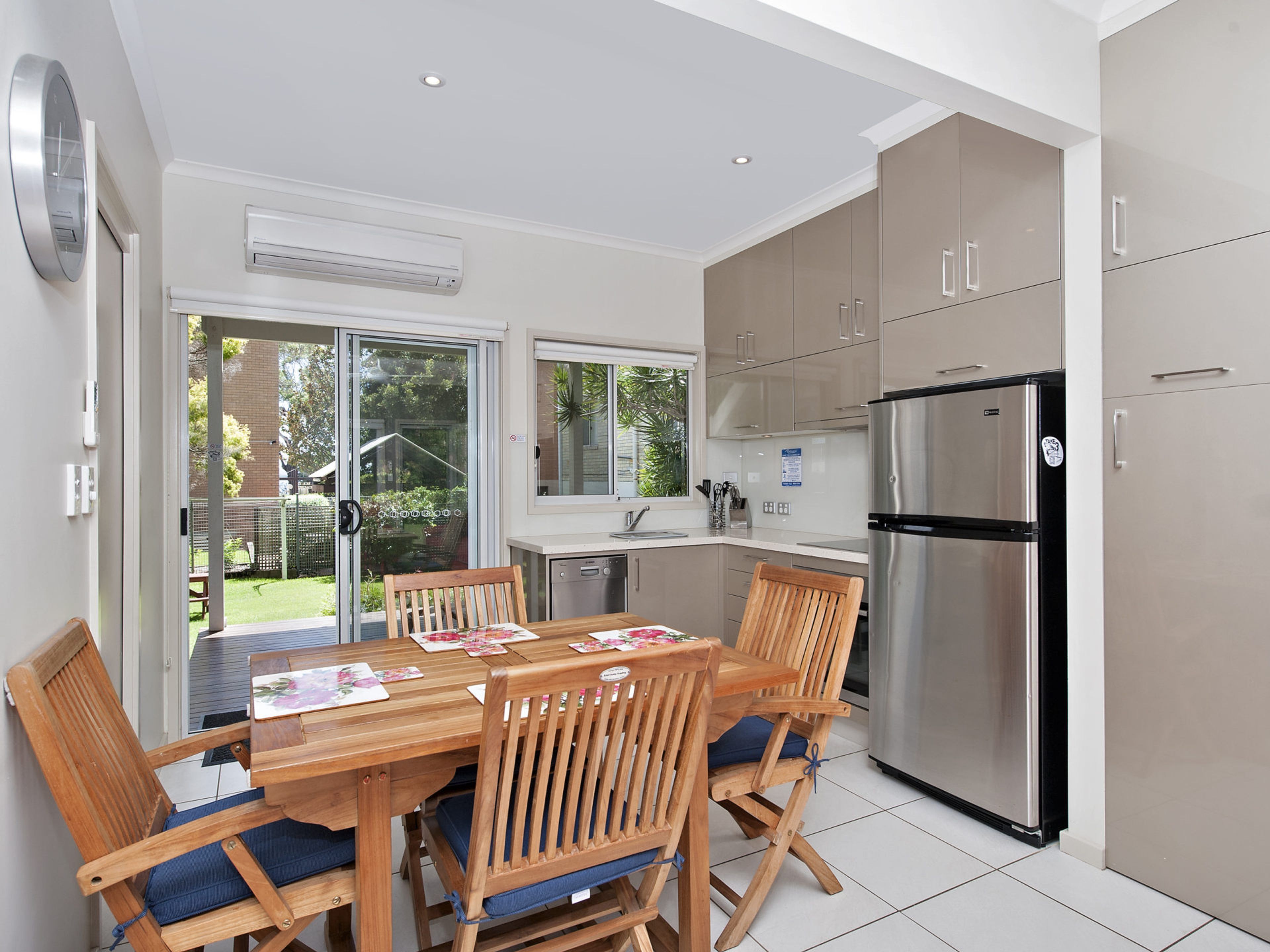 A modern kitchen with a dining table, chairs, a refrigerator, and a sliding glass door leading to a garden.