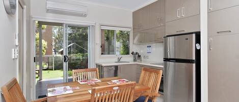 A modern kitchen with a dining table, chairs, a refrigerator, and a sliding glass door leading to a garden.