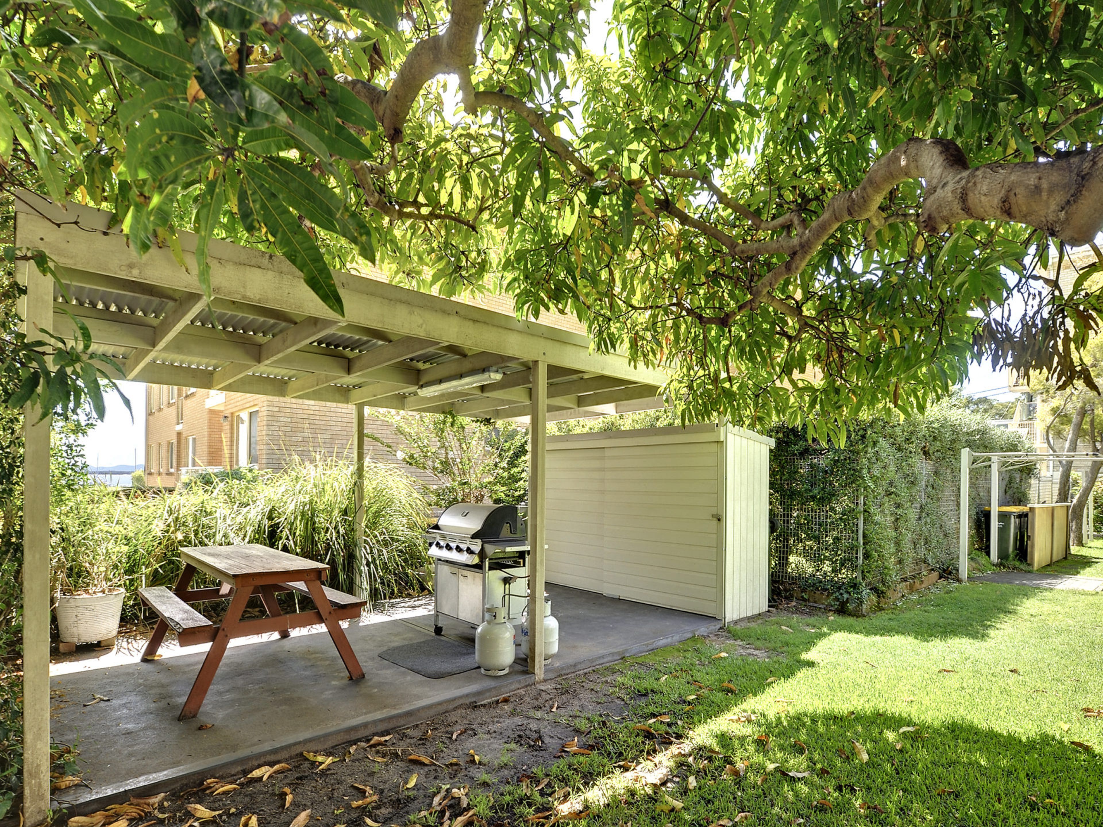 A covered outdoor area with a grill, a table, and a shed.
