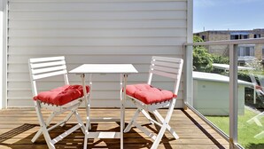 A balcony with two white chairs and a small table, overlooking a grassy area and buildings. - Florida Shoal Bay Townhouse near Beach (Shoal Bay)