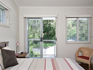 A bedroom with a bed, a chair, a nightstand, and a window with a view of greenery.