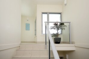 A staircase with a glass railing leading to a landing, a potted plant on the landing, and a wall with a light switch.