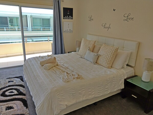 A bedroom with a large bed, a nightstand, a window with curtains, and a wall with motivational phrases.