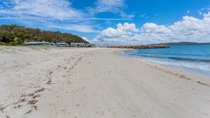 Uma praia com areal, fileira de casas e um molhe rochoso.