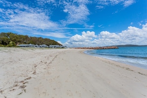 Een strand met een zandstrand, een rij huizen en een rotsenrij als kustbescherming.