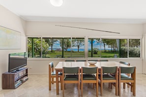 Ein Essbereich mit einem großen Tisch, Stühlen, einem Fernseher auf einem Schrank und einem Bücherregal.