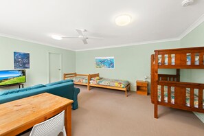 A room with a bunk bed, a sofa, a desk, and a television.