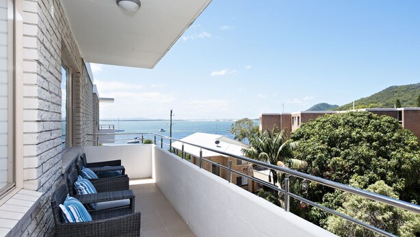 A balcony with wicker furniture, a view of the sea, and a mountain in the distance. - Del Rae, 18/25 Shoal Bay Rd - Air-conditioned, renovated 2-bedroom unit opposite Shoal Bay Beach (Shoal Bay)