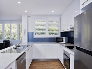 Eine moderne Küche mit weißen Schränken, einem Edelstahl-Kühlschrank, einer Mikrowelle und einem Fenster mit Jalousien.