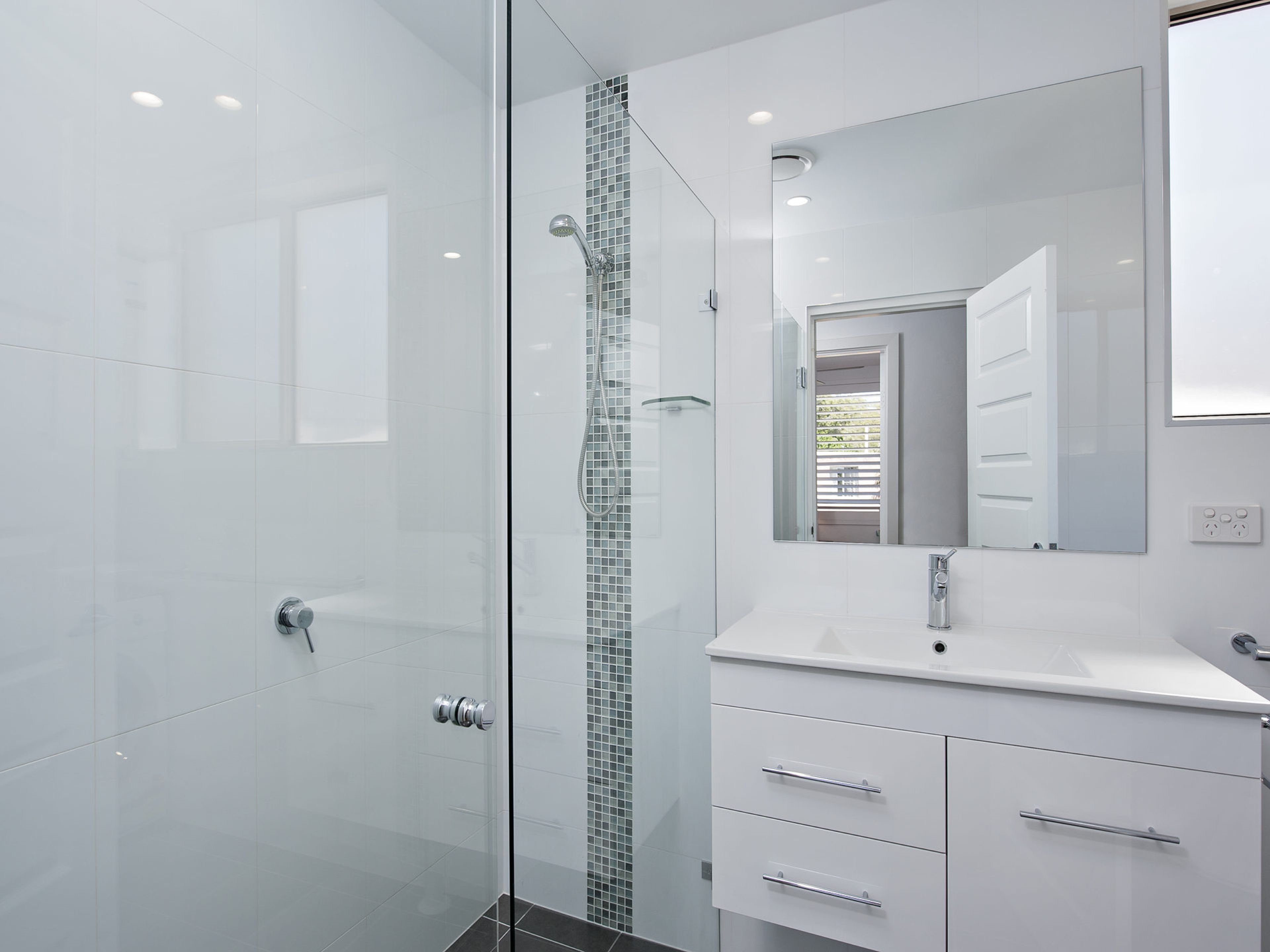 A modern bathroom with a glass shower enclosure, a white vanity with a mirror, and a tiled floor.