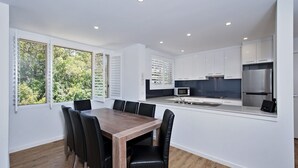 A modern kitchen with white cabinets, stainless steel appliances, and a dining area with a wooden table and black chairs. - Del Rae, 18/25 Shoal Bay Rd - Air-conditioned, renovated 2-bedroom unit opposite Shoal Bay Beach (Shoal Bay)
