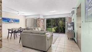 A spacious living area with a sofa, dining table, chairs, and a TV.