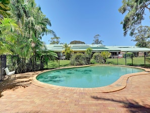 A swimming pool with a brick border, surrounded by a fence and lush greenery.