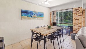 Een eetruimte met een houten tafel, zwarte stoelen, een plafondventilator en een schilderij aan de muur.