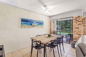 Uma sala de jantar com mesa de madeira, cadeiras pretas, ventilador de teto e um quadro na parede.