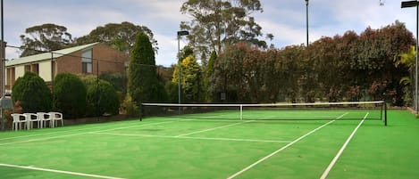 Ein Tennisplatz im Freien mit Netz, umgeben von Bäumen und einem Zaun.