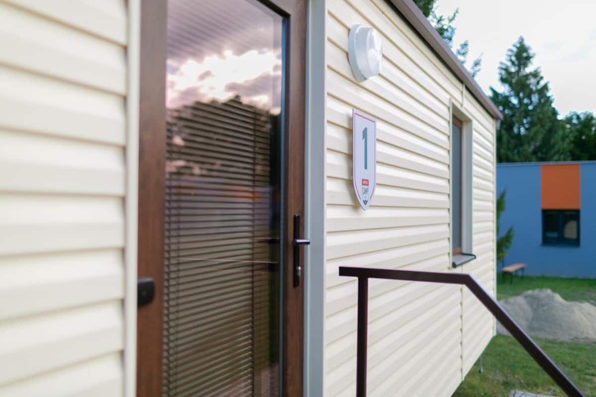 A mobile home with a sliding glass door, a small outdoor area with a bench, and a mailbox on the wall.