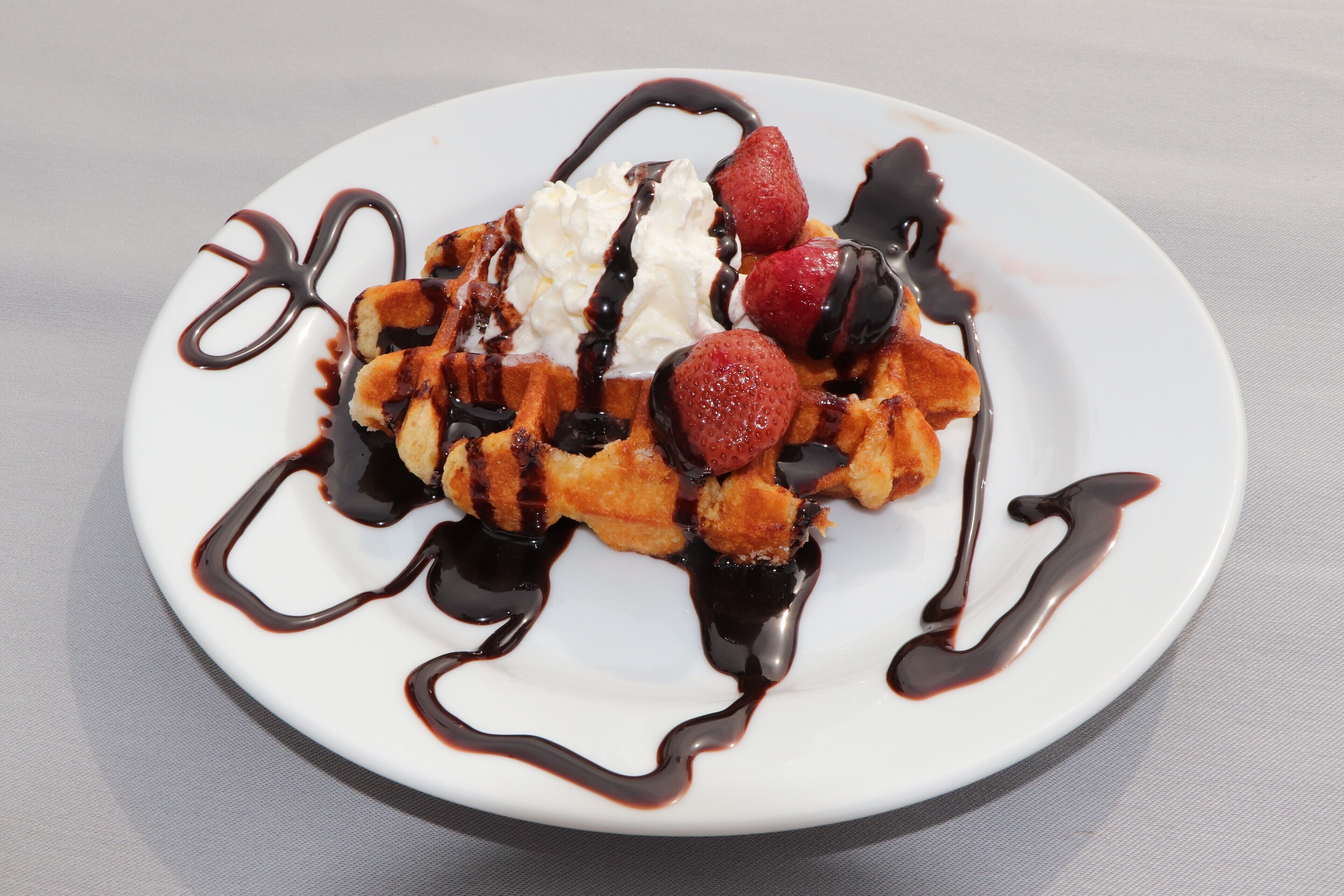 A plate of waffles with whipped cream, strawberries, and chocolate sauce.