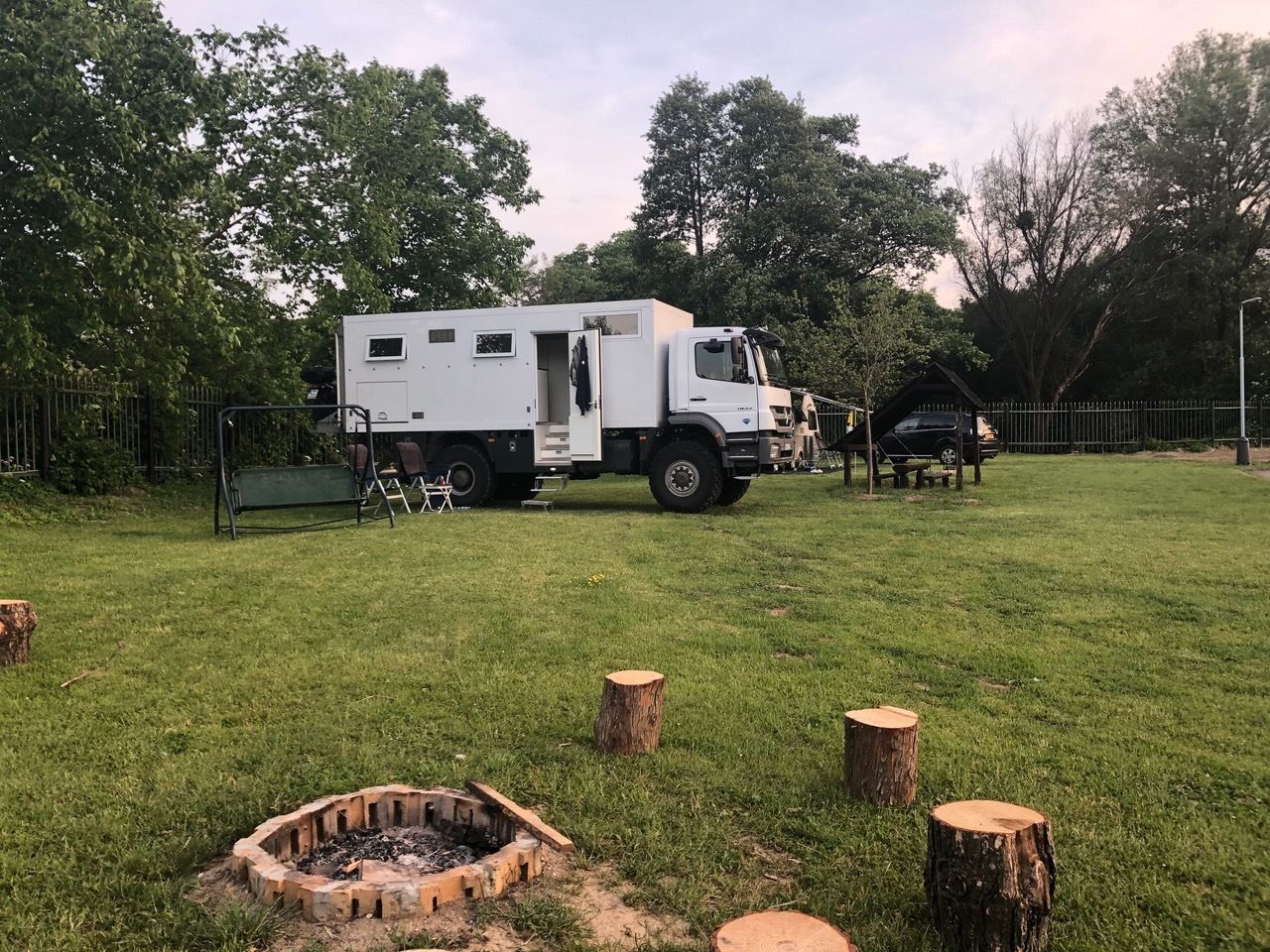 A white RV parked on a grassy field with a fire pit and wooden stumps.
