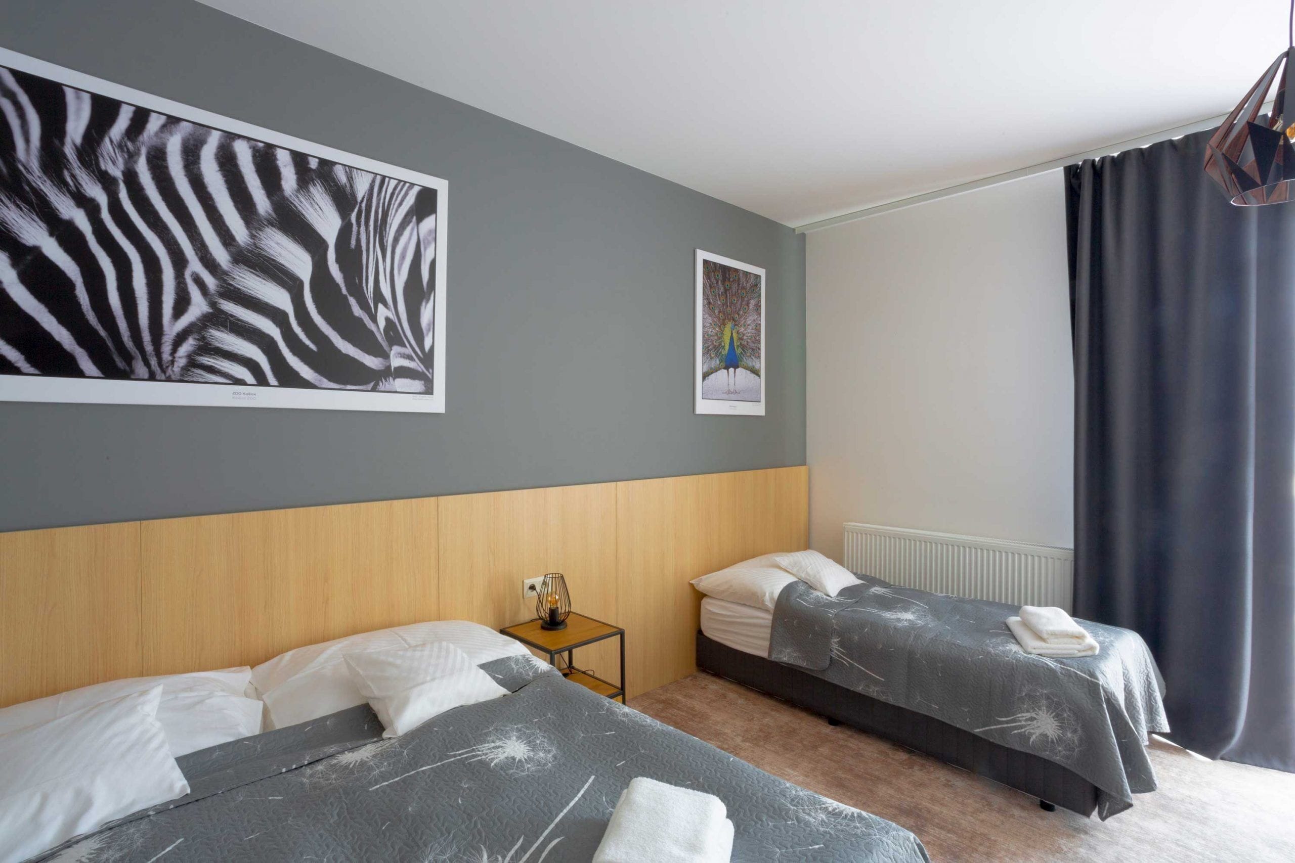Une chambre d’hôtel avec deux lits, une tête de lit en bois, une petite table avec une lampe et des œuvres d’art accrochées aux murs.