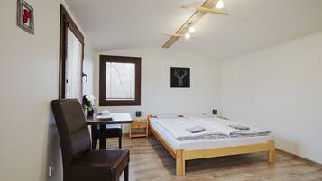 Een slaapkamer met een houten bed, een bureau met stoel, een klein tafeltje en een raam met luxaflex.