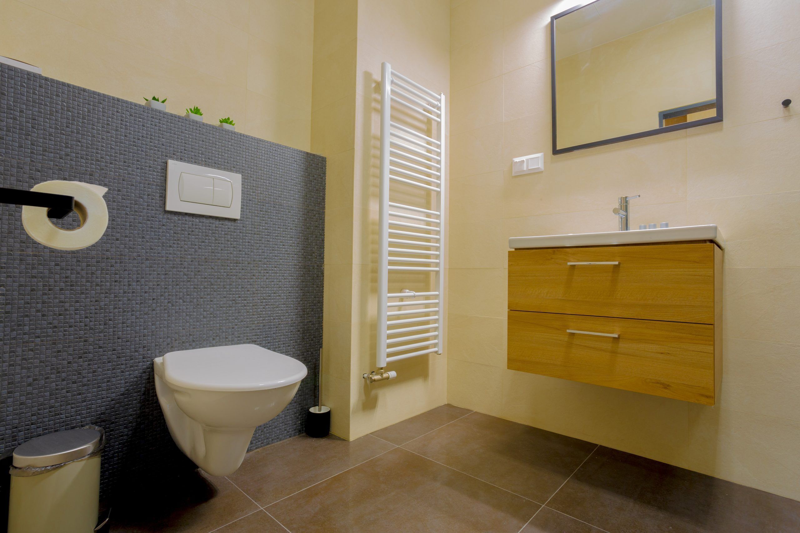 A bathroom with a toilet, a towel rack, a mirror, and a wooden vanity with drawers.