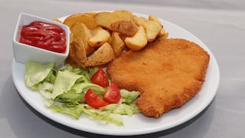 Un plato con una milanesa, cuñas de papa, lechuga y un recipiente pequeño con kétchup.