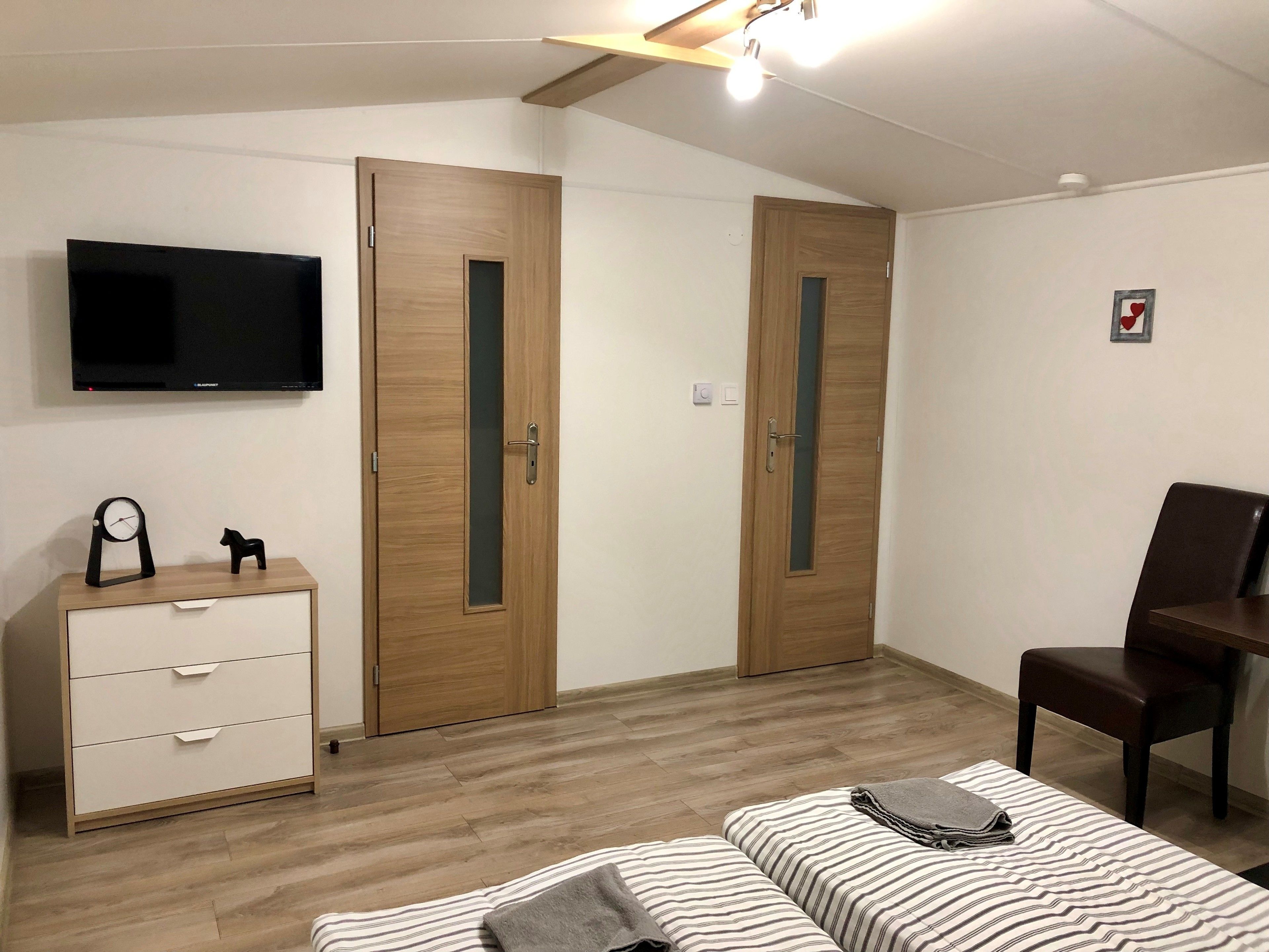 A bedroom with two wooden wardrobes, a TV mounted on the wall, a desk with a chair, and two beds with striped bedding.