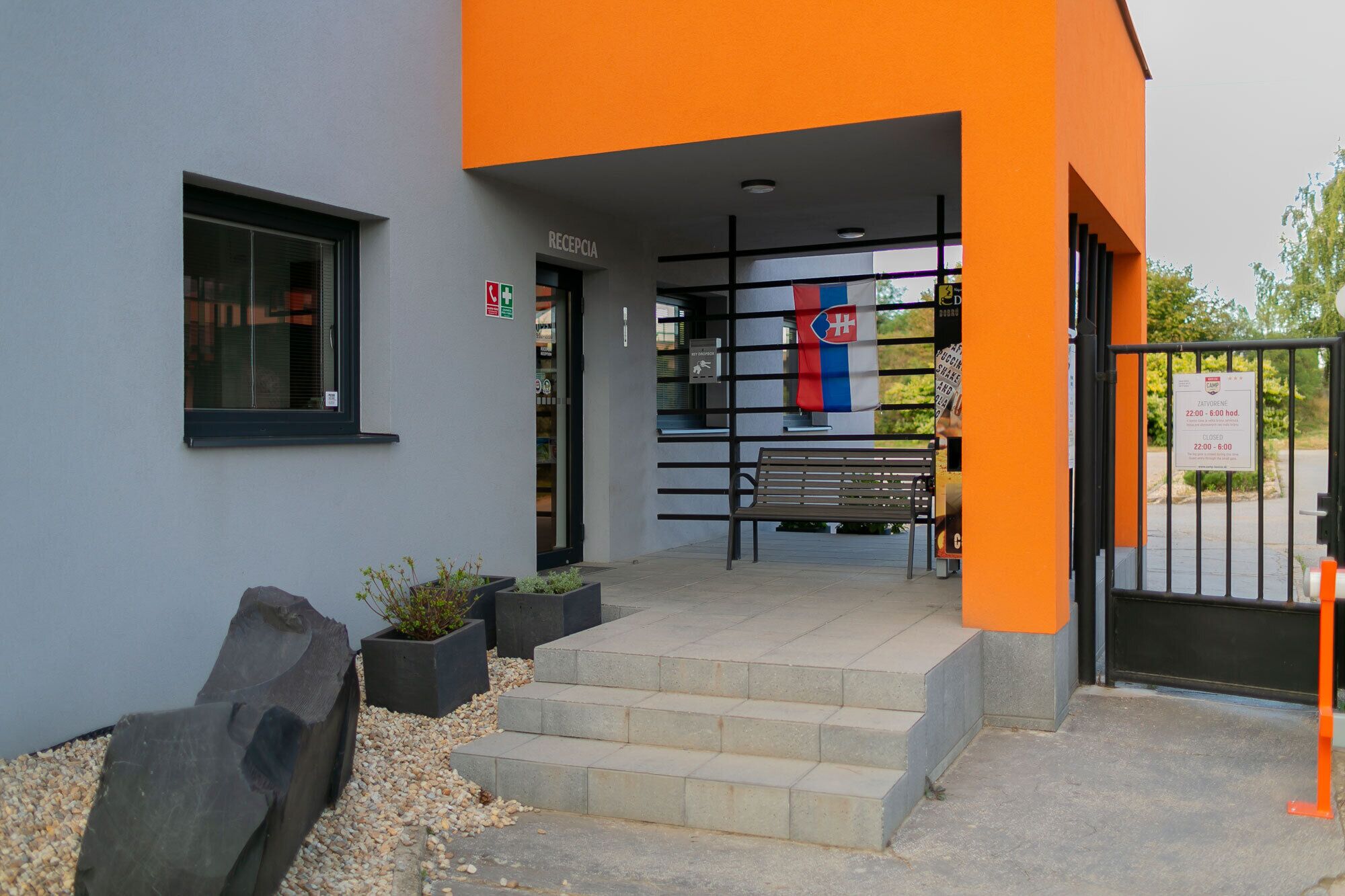 A building entrance with a reception area, steps leading up to the entrance, and a bench outside.