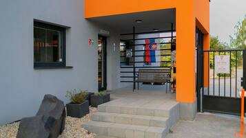 A building entrance with a reception area, steps leading up to the entrance, and a bench outside.
