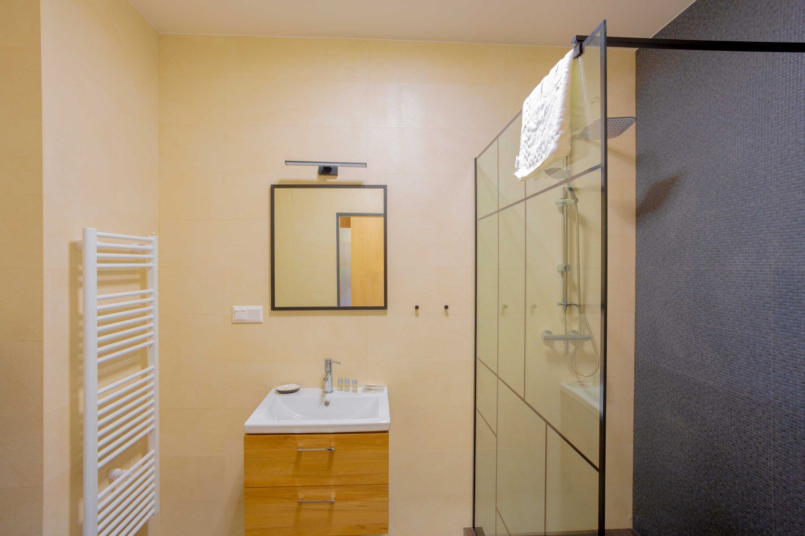 A modern bathroom with a glass shower enclosure, a white sink, and a wooden vanity.