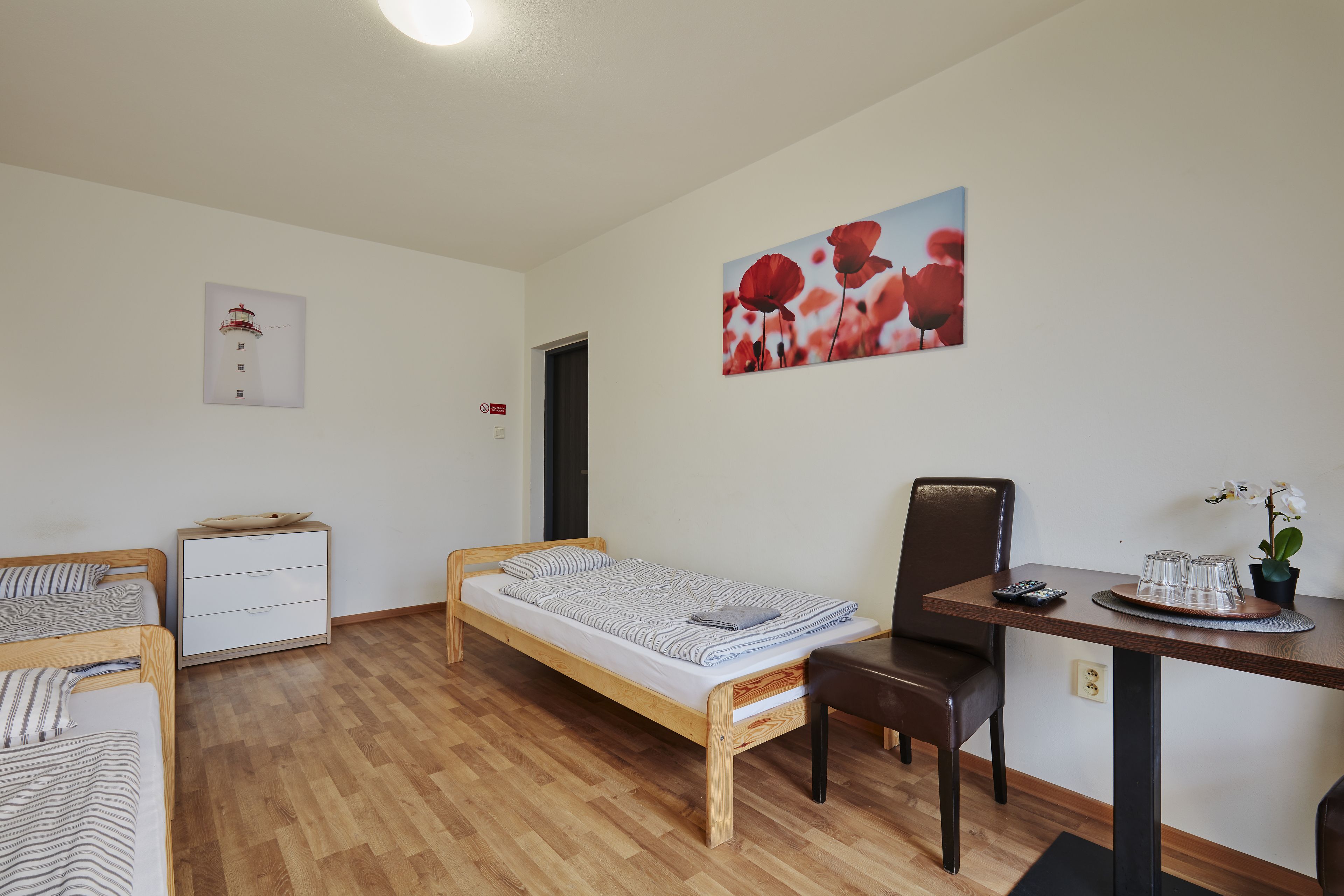 Una stanza con un letto, una scrivania, una sedia, un tavolino con bicchieri e un quadro di fiori rossi.