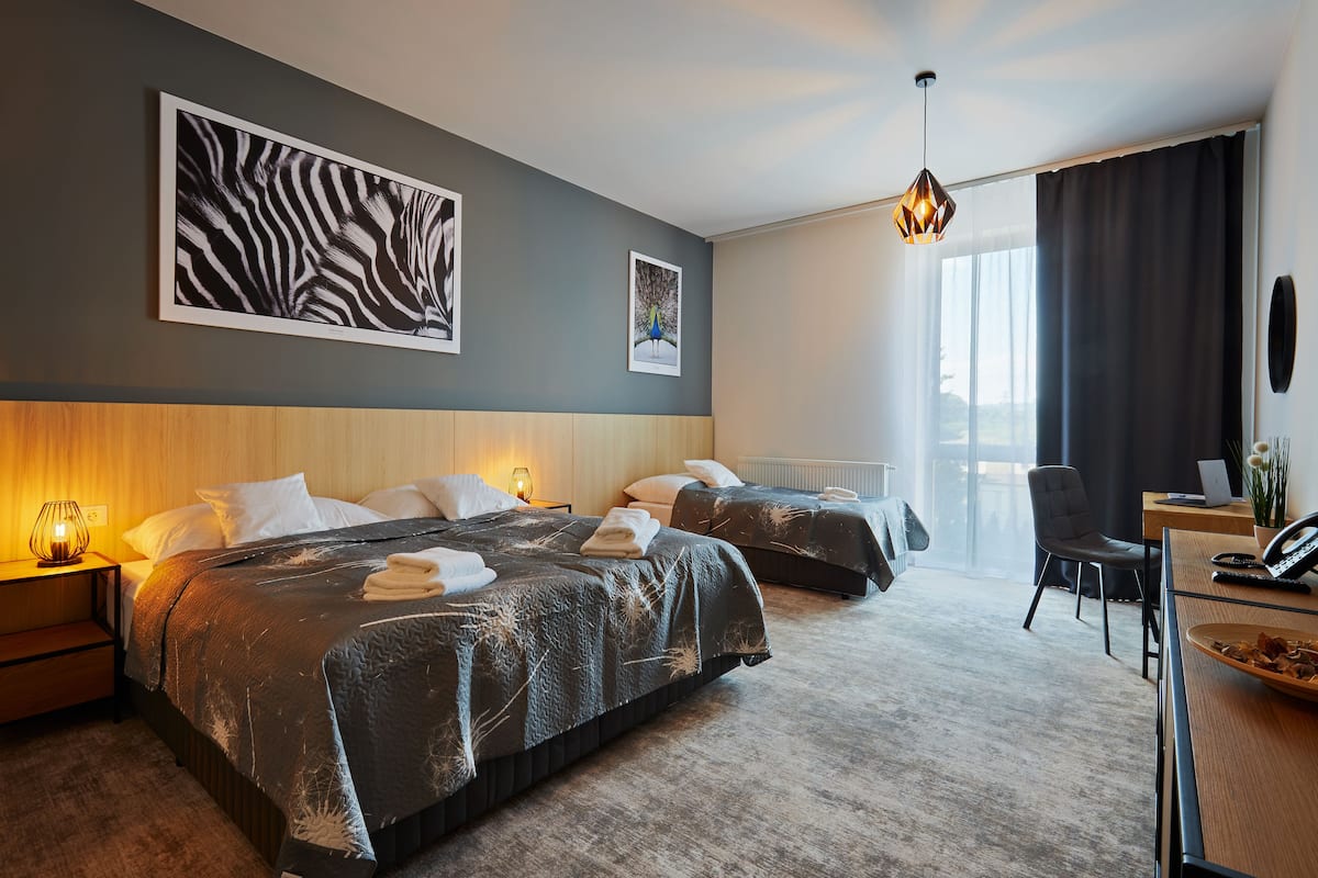 A hotel room with two beds, a desk, a chair, a lamp, and artwork on the walls.