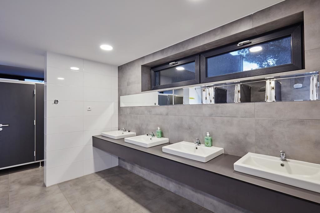 Un baño moderno con tres lavamanos, un espejo grande y una pared en tonos oscuros.