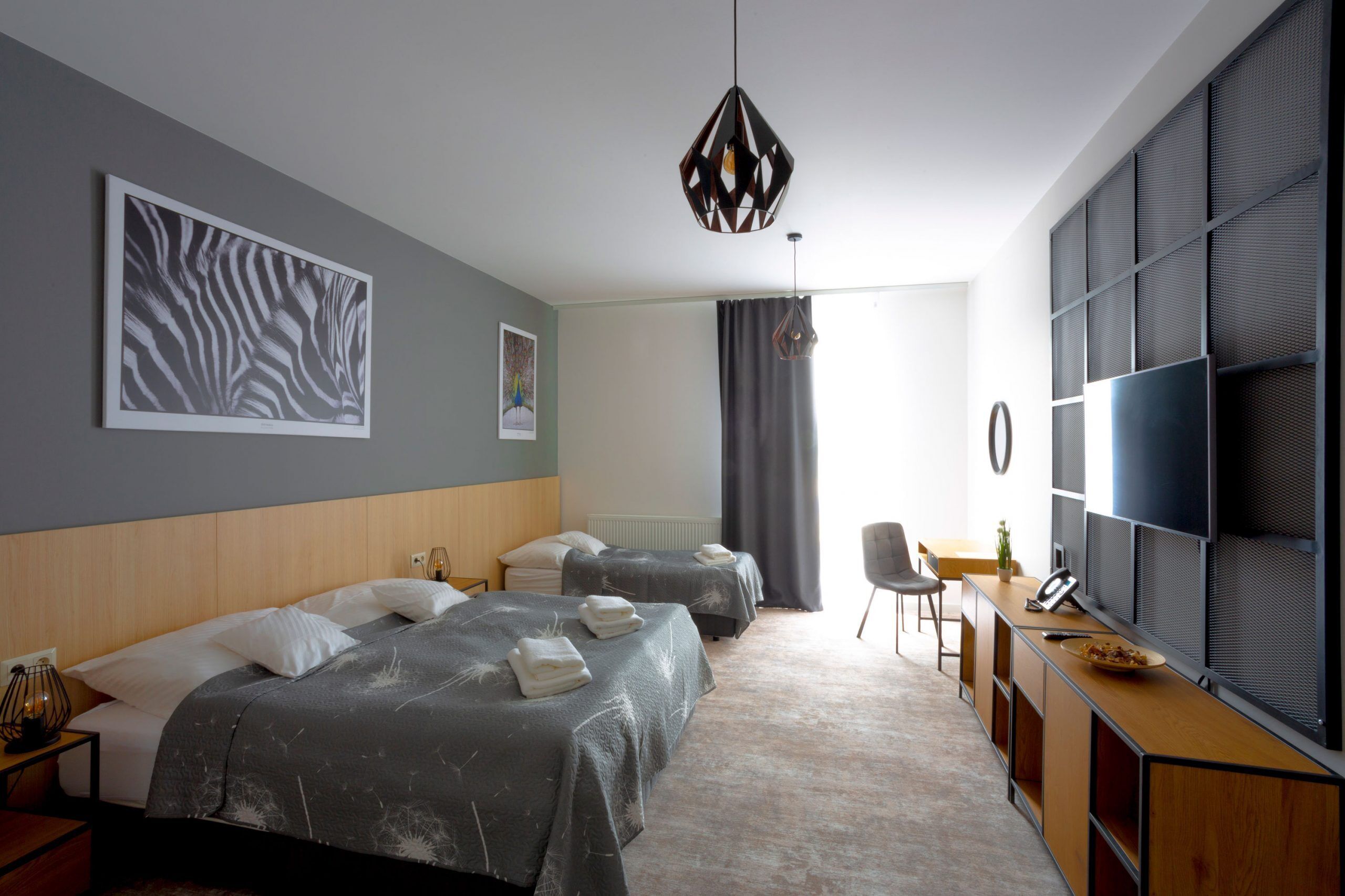 A modern hotel room with two beds, a desk, a chair, and a TV.