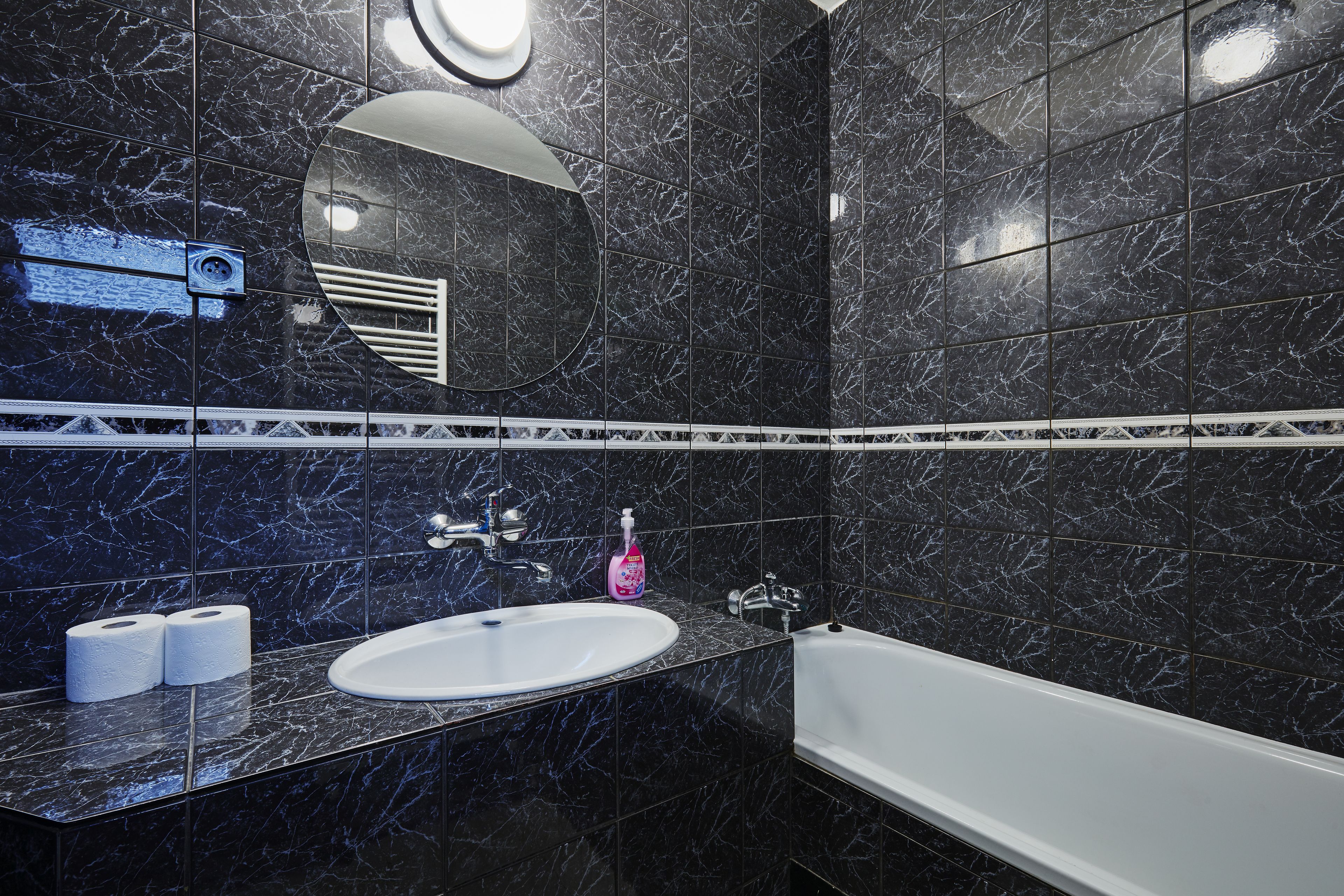 A modern bathroom with a white sink, a bathtub, and black marble tiles.