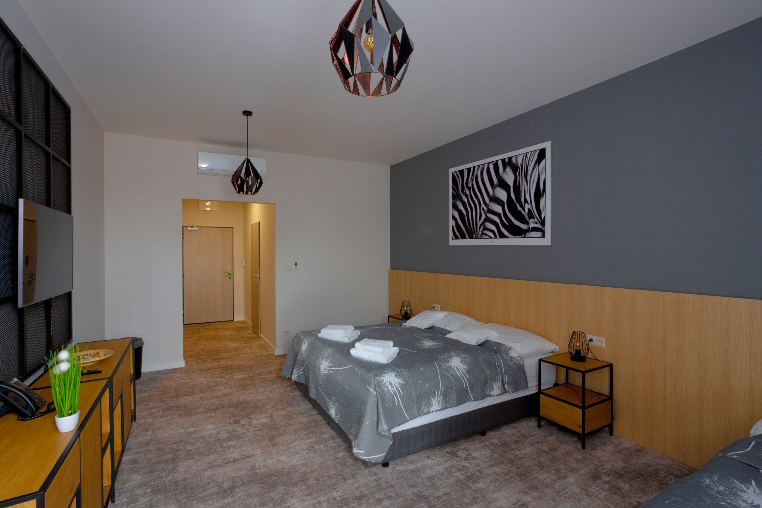 Habitació d'hotel moderna amb un llit gran, una taula de treball amb un telèfon, una petita taula auxiliar i una obra d'art amb estampat de zebra a la paret.