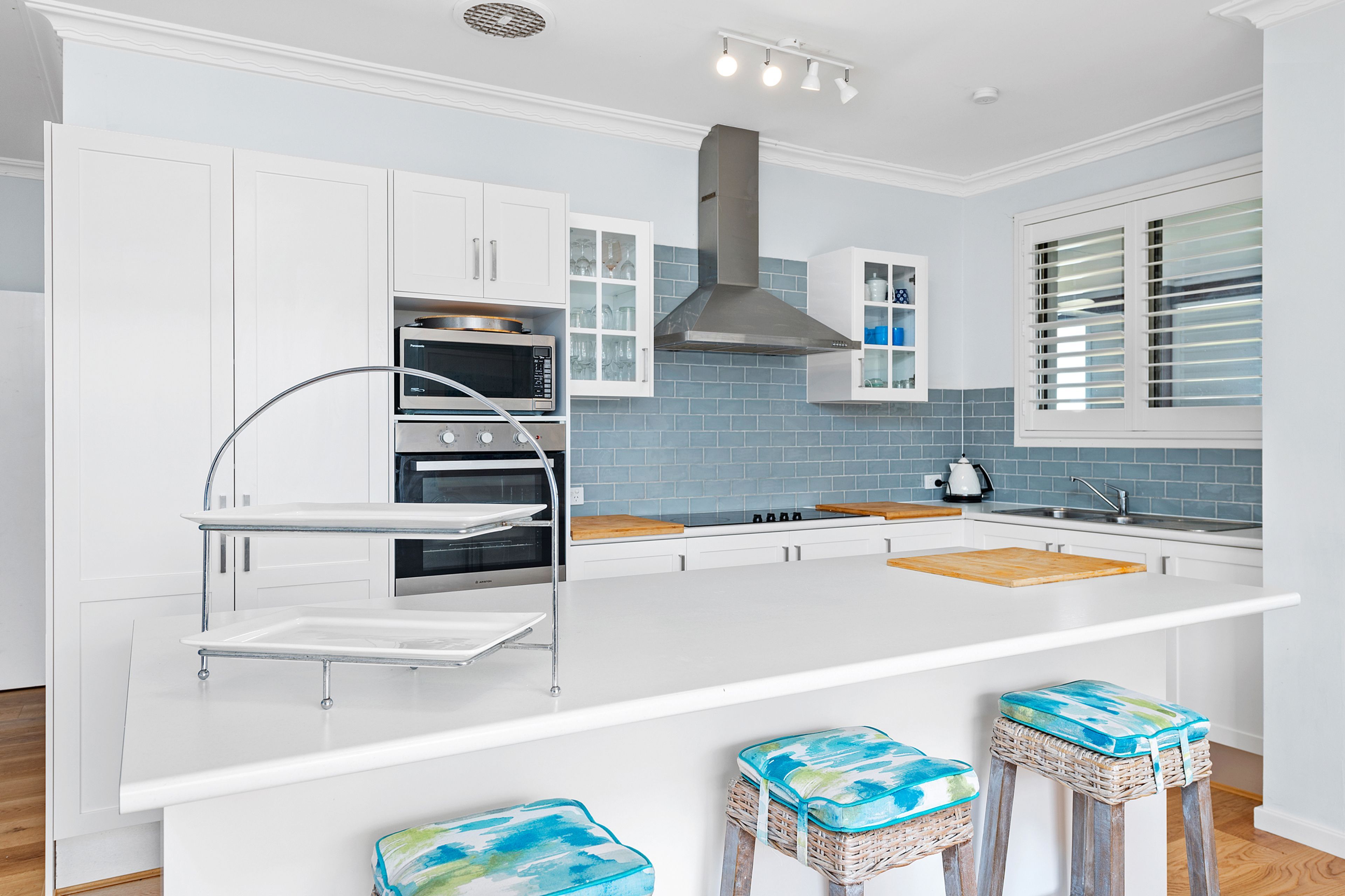 A modern kitchen with white cabinetry, a stainless steel range hood, a built-in oven, and a large island with stools.