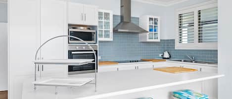 A modern kitchen with white cabinetry, a stainless steel range hood, a built-in oven, and a large island with stools.