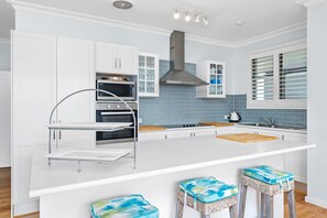 A modern kitchen with white cabinetry, a stainless steel range hood, a built-in oven, and a large island with stools.
