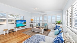 Ett rymligt vardagsrum med en stor platt-TV, en soffgrupp, ett soffbord och utsikt över havet genom stora fönster.