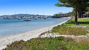A beach with boats docked in the water, a sandy shore, and a building with a green roof. - Exclusive beachfront holiday house (Soldiers Point)