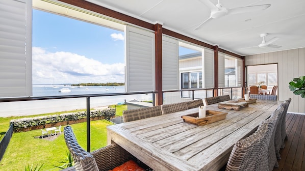 A spacious balcony with a wooden table and chairs, overlooking a marina with boats. - Exclusive beachfront holiday house (Soldiers Point)