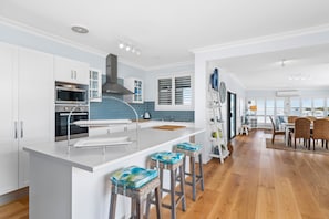 A modern kitchen with white cabinetry, stainless steel appliances, and a central island with stools. - Waterfront at Sunset Boulevard, 26 Sunset Boulevard (Soldiers Point)