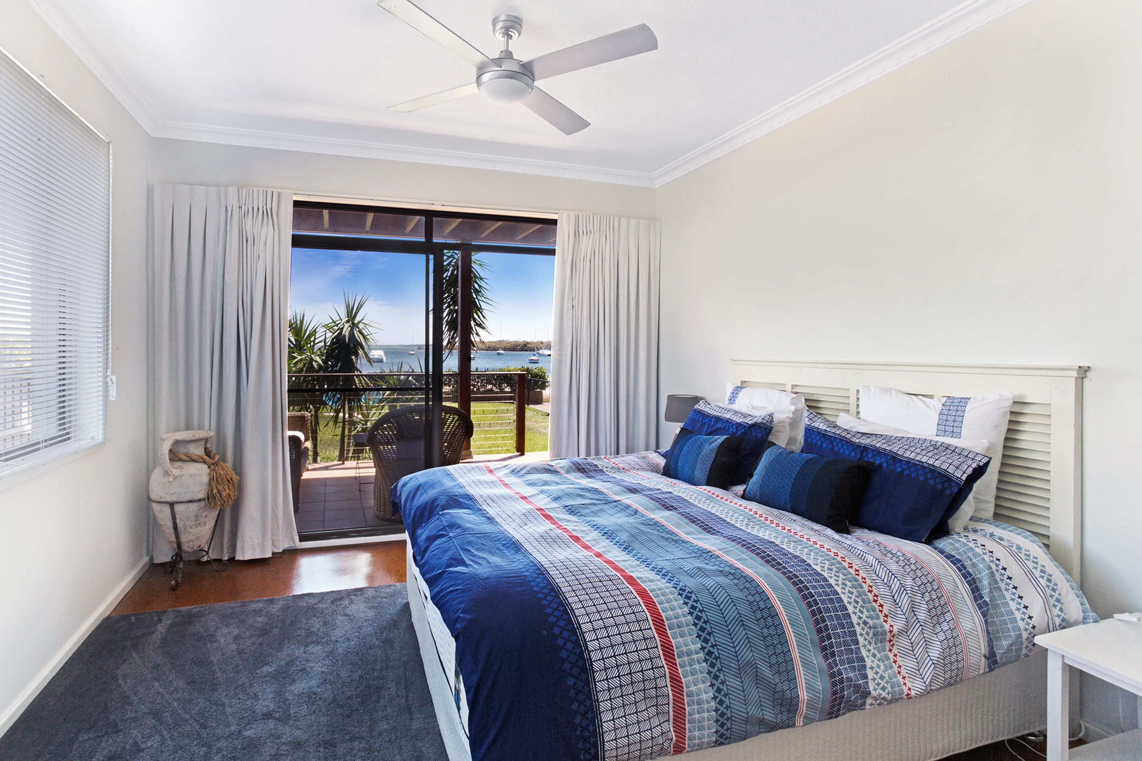 A bedroom with a bed, a ceiling fan, a view of the sea, and a balcony.