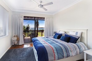 A bedroom with a bed, a ceiling fan, a view of the sea, and a balcony.
