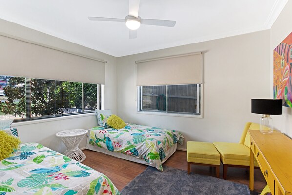 A bedroom with two beds, a desk, a chair, and a ceiling fan.